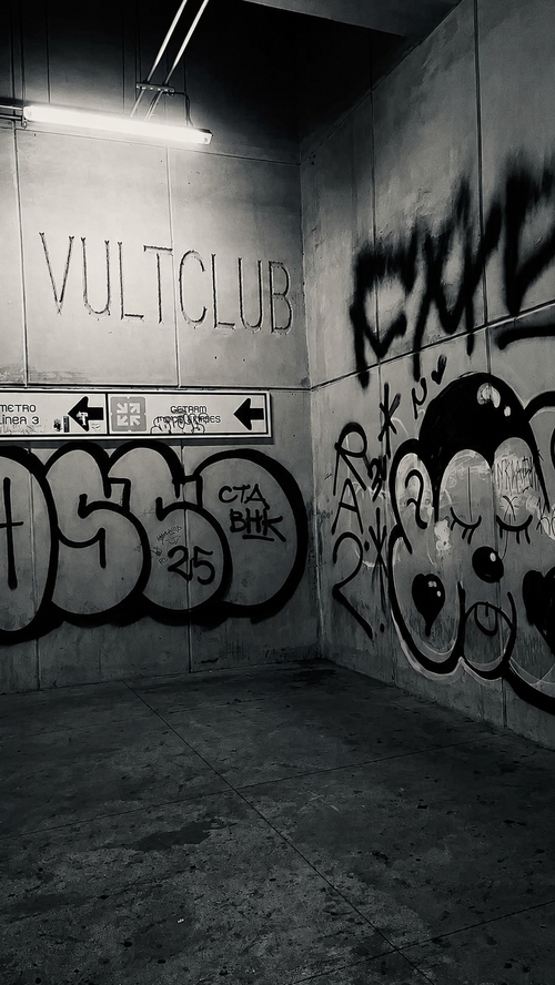 Graffiti-covered wall with 'VULTCLUB' and other text in an urban setting.